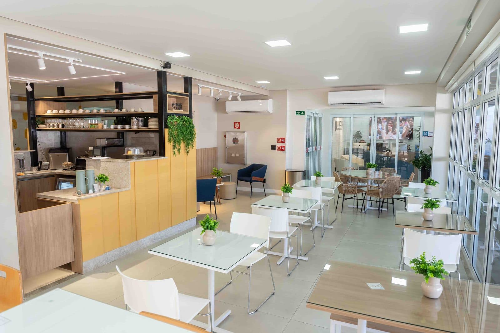 Café e coworking com balcão de madeira, mesas de estudo e parede de vidro