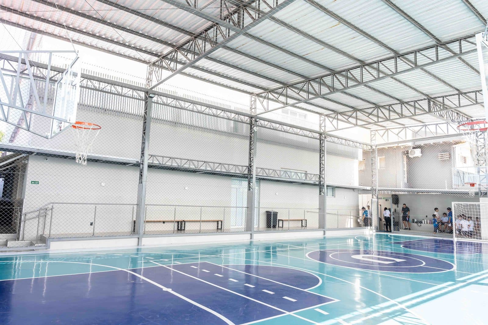 Quadra poliesportiva coberta, com piso azul e tabelas de basquete