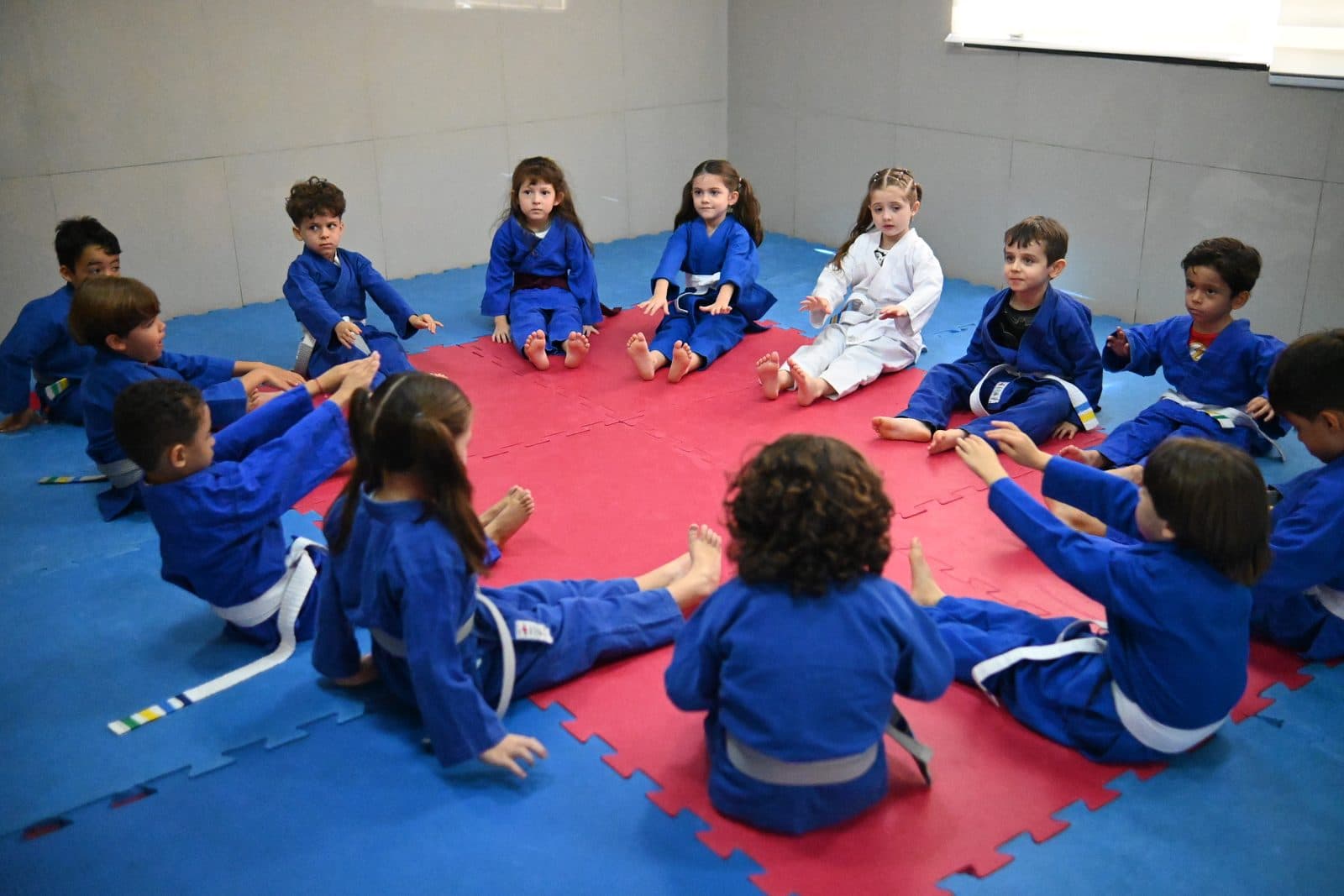 Turma de quimono azul sentada em roda no tatame da sala de judô