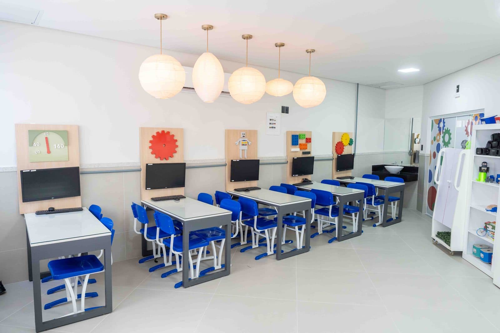 Sala de robótica com computadores sobre bancadas e cadeiras azuis